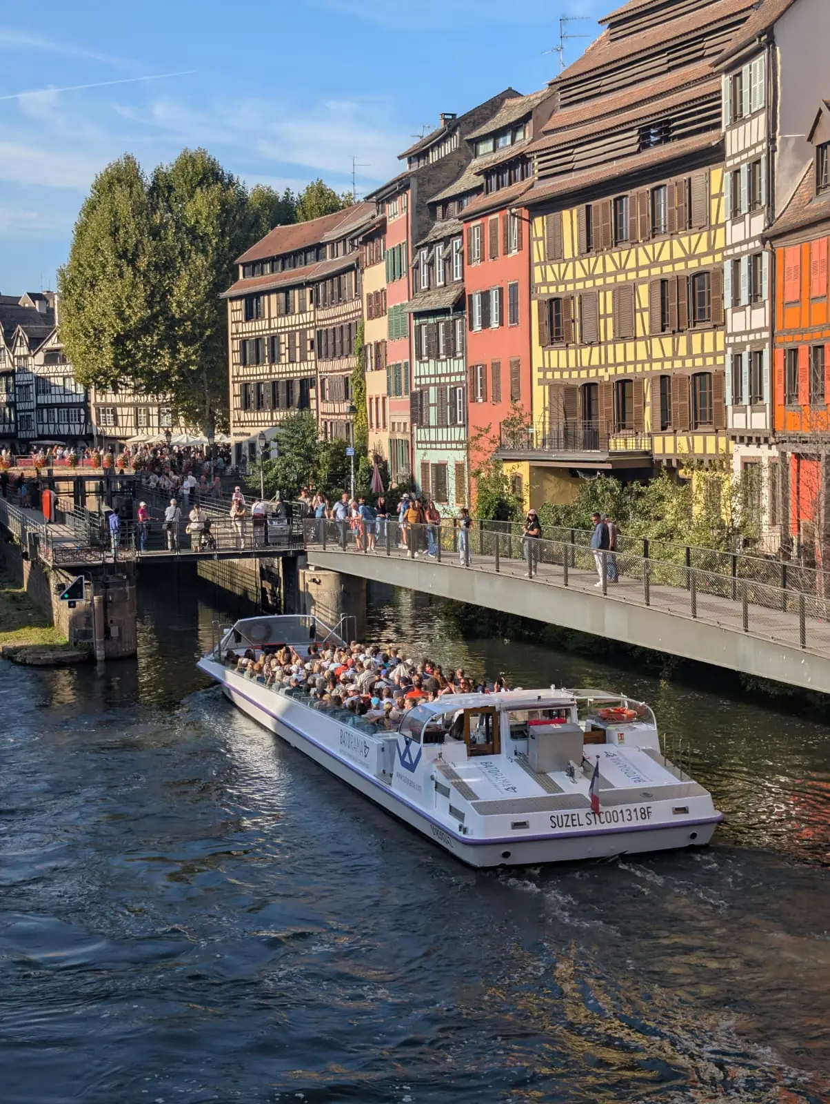 A packed tour boat entering the lock beside colourful half-timbered houses in Petite France