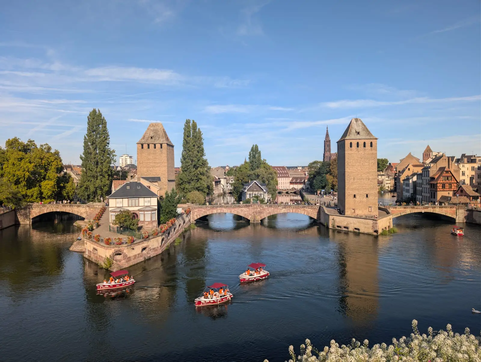 Ponts Couverts towers and bridges over the Ill, with the cathedral spire between them and small red boats on the water